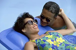 Swimwear Prints: Mature woman lying on a pool raft with a mature man beside her