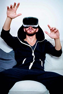 Joining Prints: Mid adult man on sofa with arms raised watching virtual reality headset