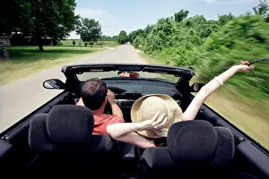Baby Boomer Prints: Middle aged baby boomer couple driving down country road in convertible with top down