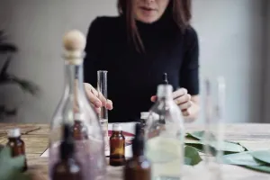 Place Of Work Prints: Midsection of female owner mixing liquid while sitting at table against wall in perfume workshop