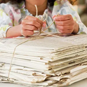 Newspaper Prints: Mixed race girl tying bundle of newspapers
