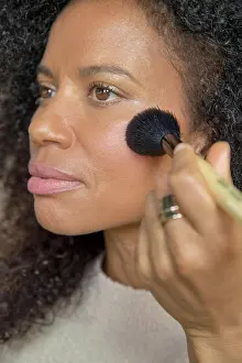 Positive Emotion Prints: Mixed race, middle-aged woman looks off camera while putting on make up