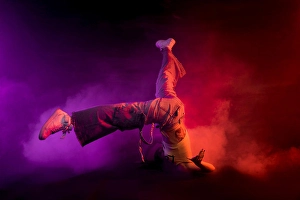 Beat Prints: Modern female performing break dance on floor in purple and red smoke on black background