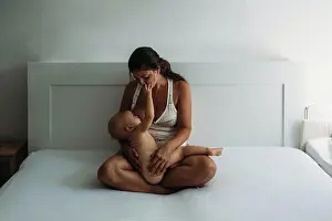 Mothers Day Prints: Mom breastfeeding while naked baby touches her face in bedroom