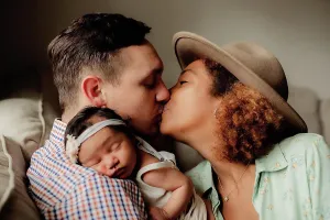 Small Group Prints: Mom and dad kissing while baby sleeps on dad's shoulder
