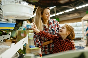 Purchase Prints: Mother with daughter choosing cage for bird at the showcase in pet store