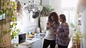 Texting Prints: Mother and daughter using smart phones in kitchen