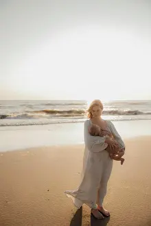 Parenting Prints: Mother holding baby on the beach by the ocean at sunset