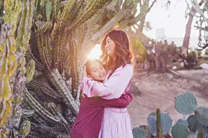Asian And Indian Ethnicities Prints: Mother hugging son in front of a big cactus with back light sun