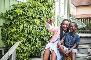 Communications Prints: Mother taking selfie through smart phone while sitting by plants on steps