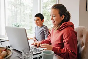 Communications Prints: Mother using laptop on table while sitting with autistic son at home