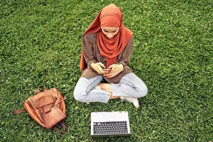 26 29 Years Old Prints: Muslim woman siting on the grass using a computer and phone