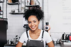 Nahaufnahme Prints: Nahaufnahme einer jungen lächelnden Barista mit lockigem Haar und Schürze Close-up of a young smiling barista with
