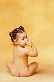 Blacks Prints: Naked African-American baby sits in a studio with her back to the camera and looks over her shoulder