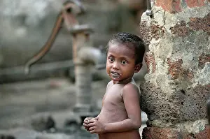 4 5 Years Prints: A naked child standing against a wall with a water hand pump in the background; Gopinathpur Village