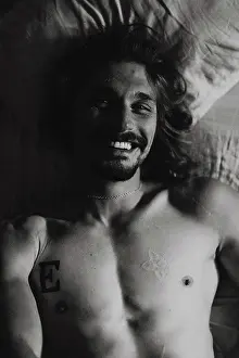 Tattoo Prints: Naked young man is looking at camera while lying in bed