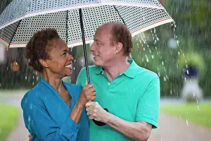 Afternoon Prints: Older couple walking through park with umbrella in the rain