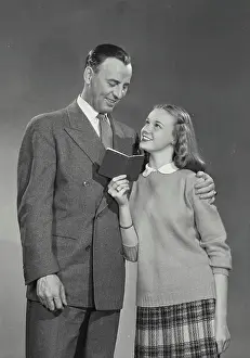 Sweater Prints: Older man in suit with arm around teenage girl wearing sweater and skirt holding small note book looking up smiling