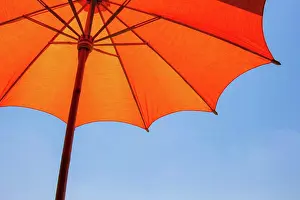 Weather Prints: Orange color beach umbrella made of wooden for protected sunlight with a bright blue sky background