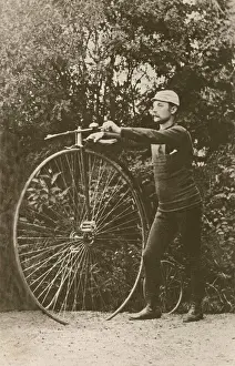 Manly Prints: Penny farthing bicycle. A man is standing beside a penny-farthing bicycle
