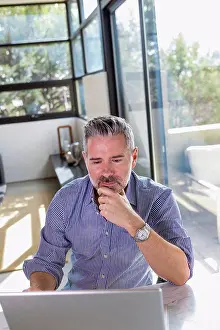 Baby Boomer Prints: Pensive Caucasian man sitting at table using laptop