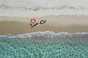 Aerial Prints: Person standing on the beach drawing a heart in the sand with aerial ocean view