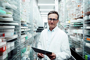 Competence Prints: Pharmacist with tablet PC standing in storage room at pharmacy