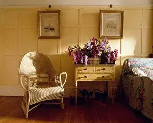 Chairs Prints: Pictures on cream panelled walls of country bedroom with wicker armchair and flowers on small antique table