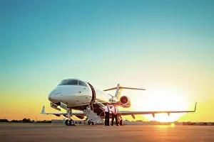 Business Travel Prints: Two Pilots standing next to Jet on tarmac of small airport at sunset