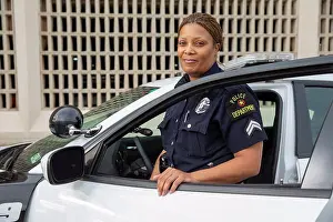 Apparel Prints: Policewoman standing in door of Police car looking towards camera smiling