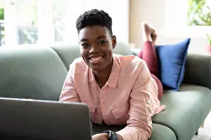 Lockdown Prints: Portrait of african american woman lying on couch using laptop working from home