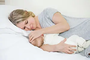 Kindergarten Prints: Portrait of a beautiful young smiling mother lying giving breast to her baby
