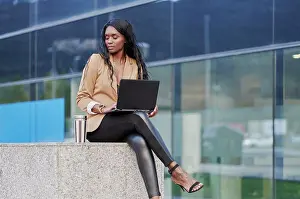 Attractive Prints: Portrait of a black executive woman sitting in a brown suit talking on the phone and holding a laptop