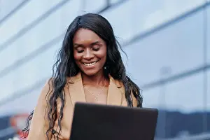 Suit Prints: Portrait of black woman wearing a brown suit working on her laptop in the street