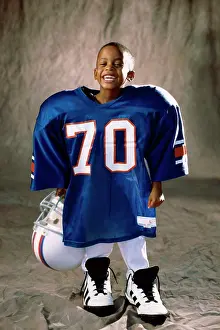 Toughness Prints: Portrait of a boy in an oversized football uniform holding a helmet