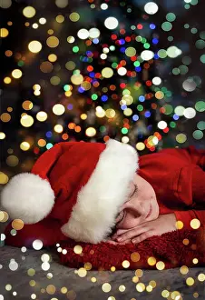 Festive Prints: Portrait of boy wearing Santa hat sleeping in front of Christmas tree