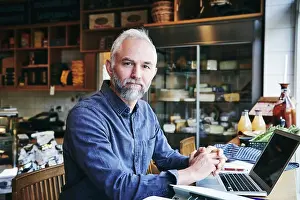 Arts Culture And Entertainment Prints: Portrait of businessman with laptop sitting at table in deli