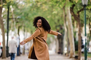 Turning Prints: Portrait carefree young woman dancing on treelined sidewalk