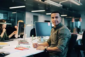 Communications Prints: Portrait of confident businessman sitting at desk while female colleagues working in creative office