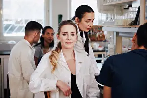 Instruction Prints: Portrait of confident young female student sitting against teacher friends in chemistry laboratory