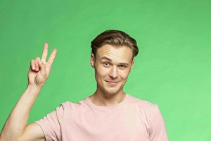 Making A Face Prints: Portrait confident young man gesturing peace sign on green background