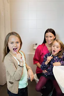 Vertically Prints: Portrait of girl brushing teeth with mother and daughter in bathroom