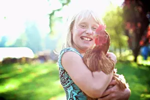 Blond Hair Prints: Portrait happy girl holding hen in sunny yard
