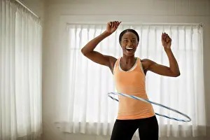 20 To 25 Years Prints: Portrait of a happy young woman hula hooping in her living room