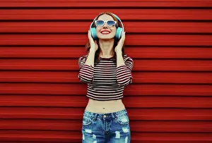 Nahaufnahme Prints: Portrait of happy young woman with wireless headphones listening to music on a red background Portrait of happy young