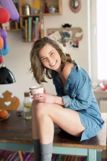 Exhilaration Prints: Portrait of laughing woman sitting on kitchen table with coffee mug