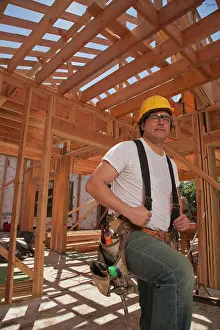 Verticals Prints: Portrait of a man wearing a hard hat and a tool belt while standing on the construction site