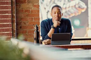 Group Of People Prints: Portrait of mixed race young man working on a tablet at an outdoor cafe, looking at camera