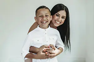 Hispanic Prints: Portrait of mother hugging son from behind and smiling in studio