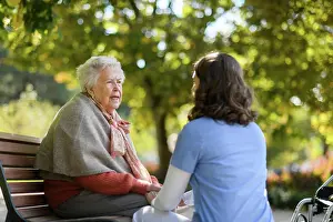 Sicherheitstechnischen Prints: Portrait of nurse and elderly woman sitting on bench in park during warm autumn day